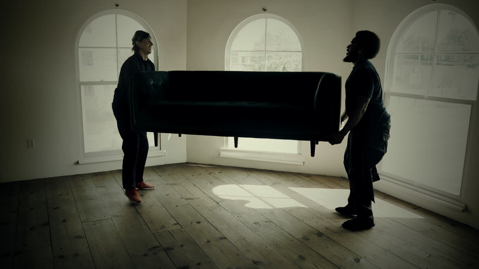 Zwei Träger heben ein Sofa durch einen hellen, leeren Raum